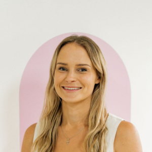 Dannielle Pickford in a white top standing in front of a pink wall smiling at the camera