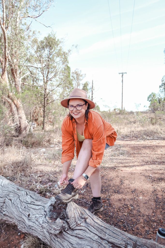 Kreete tying her hiking boots on a log hiking boots while looking at the camera smiling