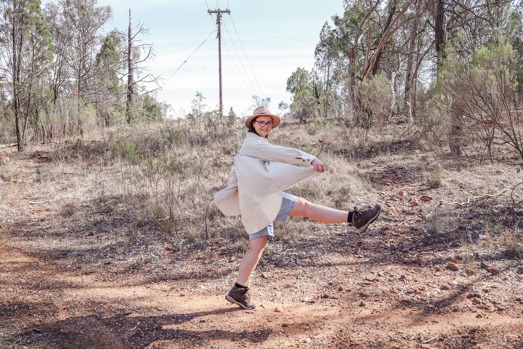 A woman in a white shirt and a hat is enthusiastically walking on a hiking trail.