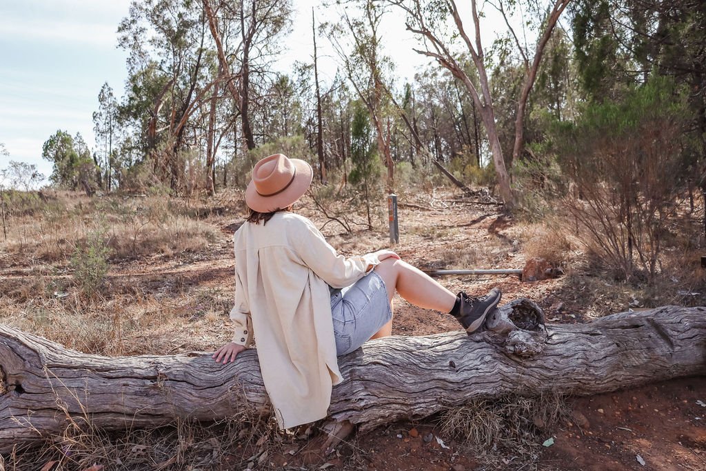 A woman enjoying an adventure sitting on a log in the middle of a field looking in the distance