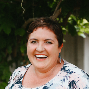 Rochelle Olsen smiling in front of a tree, smiling wide looking at the camera.
